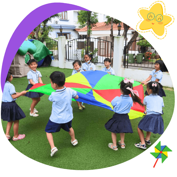 Preschool children at Starshine Montessori playing with a colourful parachute outdoors, promoting teamwork, motor skills, and joyful learning in a Montessori environment.
