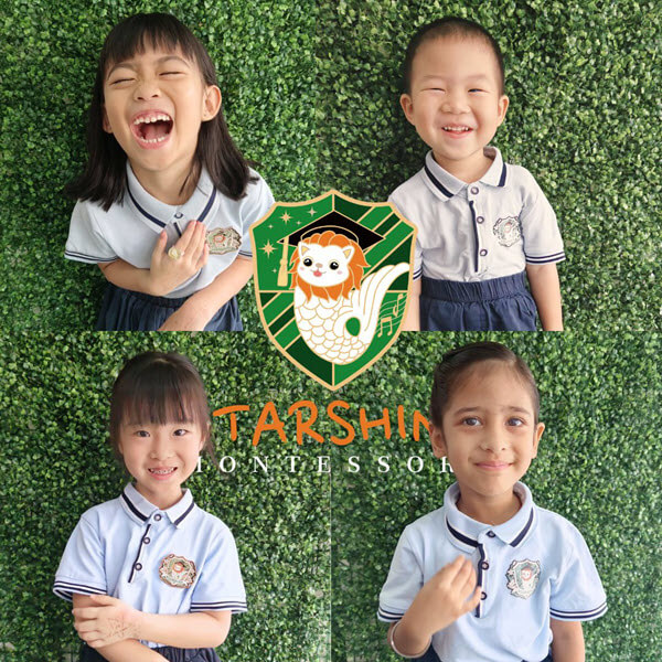 Happy preschool children in Starshine Montessori uniforms posing in front of the school logo wall in Singapore.